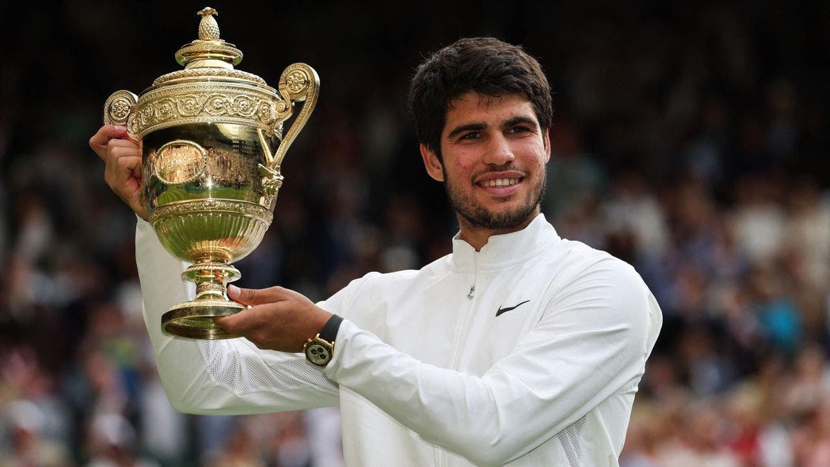 Carlos Alcaraz, en un momento de triunfo, levantando con orgullo la copa del Grand Slam tras un torneo exitoso. Alcaraz, sin enfrentarse a Djokovic, se prepara para su siguiente reto en Toronto.