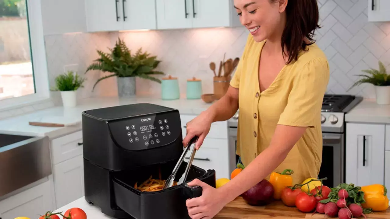 Mujer disfrutando de cocinar con su freidora de aire de MediaMarkt en la cocina de su casa.