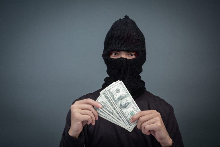 Hombre encapuchado sosteniendo una faja de billetes, en alusión al reportaje "espejo público sicario".