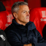 Fran Escribá sentado en el banquillo con una chaqueta azul oscura, mostrando un gesto serio y concentrado durante un partido.