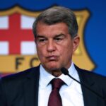 Joan Laporta, presidente del FC Barcelona, hablando en una rueda de prensa frente a un micrófono, con el escudo del club difuminado al fondo.