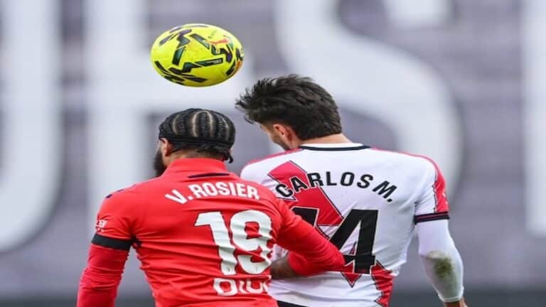 Osasuna asalta Vallecas ante Rayo Vallecano en LaLiga EA Sports con un triunfo decidido en el añadido Un partido igualado durante muchos minutos se resolvió por eficacia visitante y gestión emocional en el tramo final El duelo en Vallecas dejó una lectura clara sobre competitividad y gestión de finales de partido. Osasuna golpeó cuando más duele y se llevó tres puntos de enorme valor. El Rayo Vallecano dominó la posesión durante muchos tramos, pero no tradujo ese control en ventaja real. El encuentro se mantuvo abierto hasta el último suspiro. La eficacia navarra fue determinante. El marcador no refleja todo lo ocurrido sobre el césped. Osasuna golpea primero y castiga la falta de contundencia local tras un inicio con dominio territorial del Rayo El arranque fue de iniciativa local, con el Rayo Vallecano tratando de instalarse en campo rival mediante posesiones largas. Sin embargo, el primer golpe llegó del lado visitante. En el minuto 29, Ante Budimir aprovechó una acción bien trabajada para adelantar a Osasuna, culminando una asistencia precisa de Herrando. El tanto asentó al conjunto rojillo, que supo bajar el ritmo del partido y gestionar los espacios. El Rayo mantuvo el balón, pero le costó generar ocasiones claras ante una defensa bien organizada. La primera parte se cerró con sensación de control visitante pese al empuje local. Tras el descanso, el escenario cambió. El Rayo subió líneas y encontró premio en el minuto 60. Pathé Ciss firmó el empate tras una acción colectiva bien interpretada, con Isi Palazón como asistente. Vallecas empujó y el partido entró en una fase de intercambio de golpes y tensión creciente. El tramo final y el VAR marcan el desenlace con dos goles tardíos que sellan la victoria rojilla Cuando el empate parecía definitivo, Osasuna mostró mayor claridad emocional. En el minuto 91, Víctor Muñoz apareció para firmar el 1 a 2 tras una jugada rápida que castigó el desajuste local. El Rayo acusó el golpe y dejó espacios en su intento desesperado por igualar. Poco después llegó la acción más controvertida. El VAR revisó una posible pena máxima a favor de Osasuna, pero el árbitro mantuvo su decisión inicial. Esa revisión alargó el añadido y terminó beneficiando de nuevo a los visitantes. En el minuto 94, Asier Osambela sentenció el partido con el tercer tanto. La acción fue validada tras una nueva revisión del VAR, confirmando un desenlace cruel para el Rayo y muy rentable para Osasuna. Lectura competitiva y consecuencias clasificatorias tras un partido de dos caras bien diferenciadas El Rayo Vallecano cerró el partido con un 67 por ciento de posesión, dato que refuerza su propuesta pero también expone su falta de pegada. Osasuna, por su parte, demostró colmillo competitivo y capacidad para decidir en escenarios de máxima presión. La victoria refuerza al conjunto navarro en la clasificación y consolida su fiabilidad como visitante. Para el Rayo, el resultado deja la sensación de oportunidad perdida y la necesidad de ajustar detalles en los minutos decisivos. En partidos tan ajustados, la eficacia vuelve a marcar la diferencia. V. Rosier y Carlos M. saltando por un balón aéreo en un lance del partido entre el Rayo Vallecano y el CA Osasuna en Vallecas.