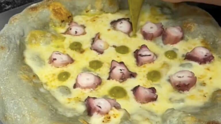 Una pizza de color azul celeste con rodajas de pulpo, queso de tetilla y crema de pimientos de Padrón.