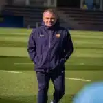 Hansi Flick, entrenador del FC Barcelona con chaqueta azul oscuro del club, caminando por el césped durante un entrenamiento matinal.