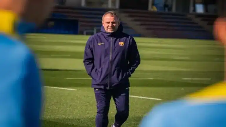 Hansi Flick, entrenador del FC Barcelona con chaqueta azul oscuro del club, caminando por el césped durante un entrenamiento matinal.
