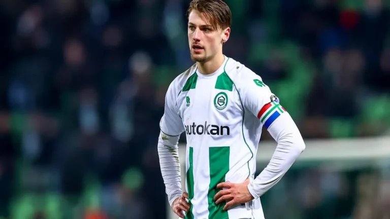 Stije Resink, joven futbolista neerlandés, con la equipación blanca y verde del Groningen, de pie en el campo con las manos en las caderas y expresión concentrada.