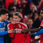 Gianluca Prestianni, jugador del Benfica, cubriéndose la boca con la camiseta mientras intercambia palabras con Vinicius Junior y Camavinga del Real Madrid en el Estadio Da Luz durante el partido de ida de los playoffs de Champions League.