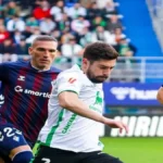 Acción del partido Eibar vs Racing de Santander en Ipurua, con jugadores del Racing con camiseta blanca y del Eibar con su clásica elástica azulgrana disputando un balón dividido.