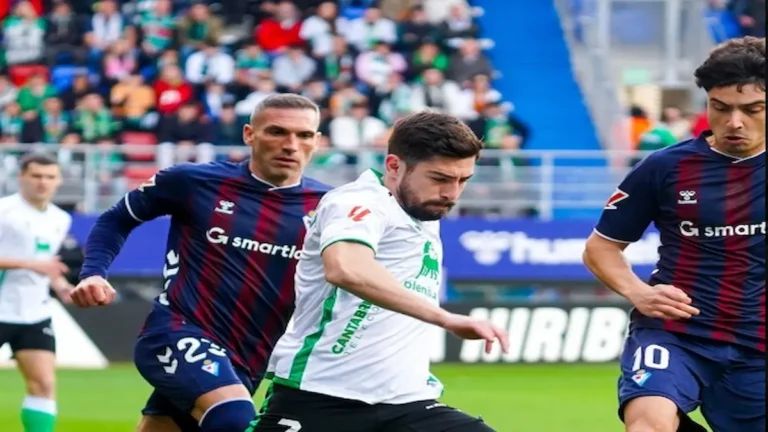 Acción del partido Eibar vs Racing de Santander en Ipurua, con jugadores del Racing con camiseta blanca y del Eibar con su clásica elástica azulgrana disputando un balón dividido.