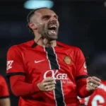 Vedat Muriqi, delantero del RCD Mallorca, celebrando un gol con un grito de euforia y los puños cerrados, vistiendo la equipación roja con detalles negros.