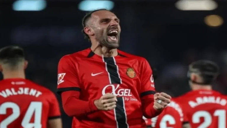 Vedat Muriqi, delantero del RCD Mallorca, celebrando un gol con un grito de euforia y los puños cerrados, vistiendo la equipación roja con detalles negros.
