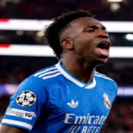 Vinícius Jr. con la camiseta azul del Real Madrid celebrando con un grito de euforia en un partido de Champions League en febrero de 2026.