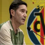 Marcelino García Toral, entrenador del Villarreal CF, hablando en rueda de prensa con el escudo del club de fondo.