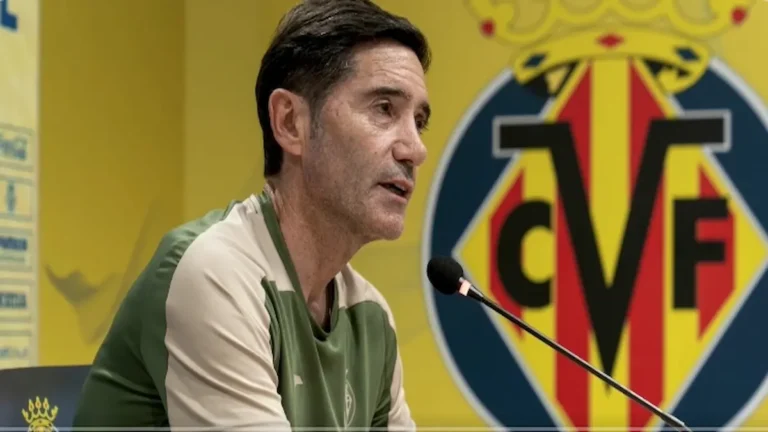 Marcelino García Toral, entrenador del Villarreal CF, hablando en rueda de prensa con el escudo del club de fondo.