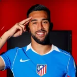 Nico González posando con la camiseta azul del Atlético de Madrid y haciendo un gesto de saludo con la mano en la frente.