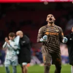 Jugadores del Real Betis celebrando la victoria en el Metropolitano mientras la grada observa con resignación.