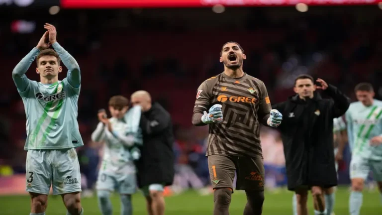 Jugadores del Real Betis celebrando la victoria en el Metropolitano mientras la grada observa con resignación.