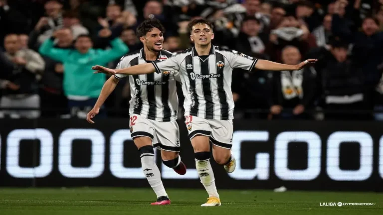 Dos jugadores del CD Castellón con la equipación albinegra a rayas verticales celebran un gol con los brazos extendidos y gestos de alegría sobre el césped del SkyFi Castalia.