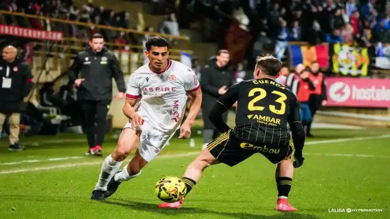 Acción de juego entre un jugador de la Cultural Leonesa con camiseta blanca 'Aspire' y un jugador del Real Zaragoza con el dorsal 23 'Cuenca' durante el partido en el Reino de León.