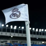 Banderín con el escudo del Real Madrid ondeando en un estadio de fútbol bajo los focos de la Champions League.