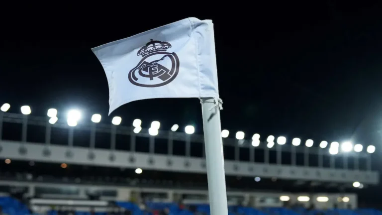 Banderín con el escudo del Real Madrid ondeando en un estadio de fútbol bajo los focos de la Champions League.