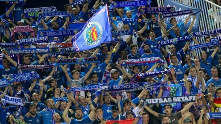 Aficionados del Getafe CF celebrando con banderas azulonas en las gradas durante un partido.