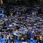 Aficionados de la Real Sociedad animando con bufandas y banderas, representando la pasión por la final de Copa del Rey.