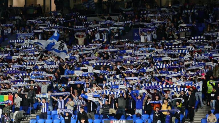 Aficionados de la Real Sociedad animando con bufandas y banderas, representando la pasión por la final de Copa del Rey.