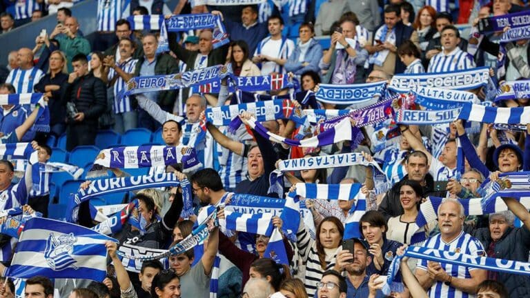 Aficionados de la Real Sociedad animando en Anoeta con banderas y bufandas antes del viaje a la final de Copa en Sevilla, marzo de 2026.