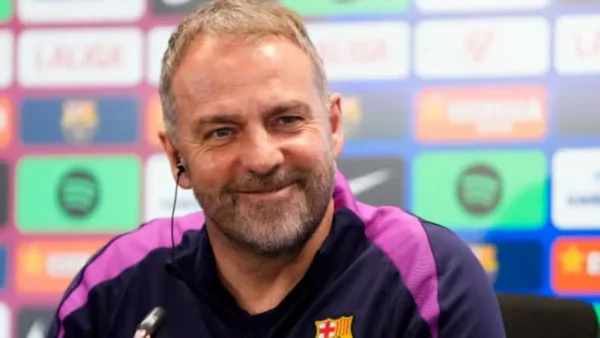 Hansi Flick sonriendo durante una rueda de prensa oficial del FC Barcelona con el panel de patrocinadores de fondo.