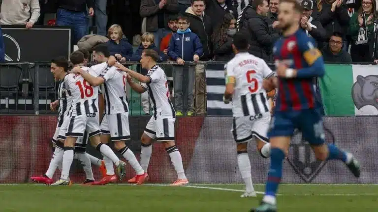Jugadores de SD Huesca y CD Castellón durante el partido en El Alcoraz, con el marcador de fondo y aficionados en las gradas.