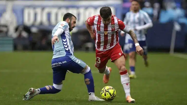 Jugador del UD Almería conduce el balón ante la presión de un defensa del Málaga CF en La Rosaleda durante la ida del playoff de ascenso a Primera División 2026