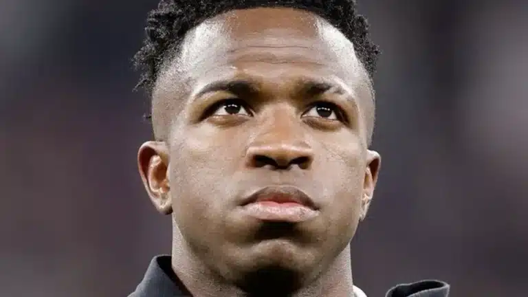 Vinícius Júnior, con chándal oscuro y gesto serio, mira al frente sobre el césped antes de un partido