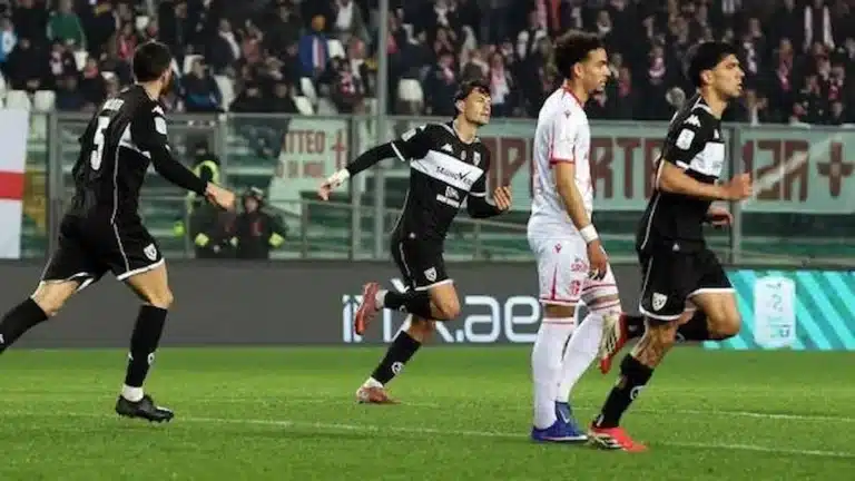 Futbolistas con camiseta negra celebran un gol ante un rival vestido de blanco y granate