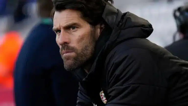 Benjamin Kugel, con chaqueta negra y barba, observa concentrado apoyado en una barandilla del banquillo durante un partido