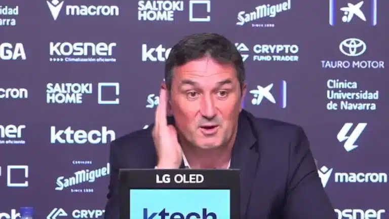 Braulio Vázquez gesticula en rueda de prensa ante los medios, fondo azul con patrocinadores de Osasuna
