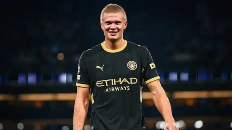 Erling Haaland, con la camiseta suplente negra y dorada del Manchester City, sonríe con un trofeo individual en la mano