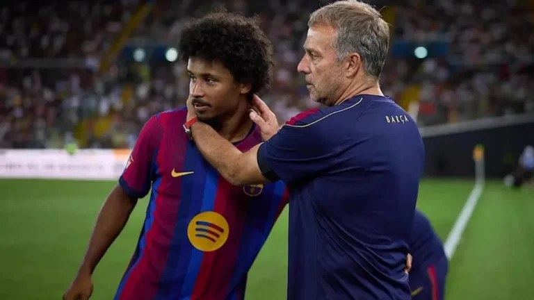 Hansi Flick, con la mano en el cuello de Karim Adeyemi, ambos con la indumentaria del FC Barcelona, en el césped durante un partido nocturno