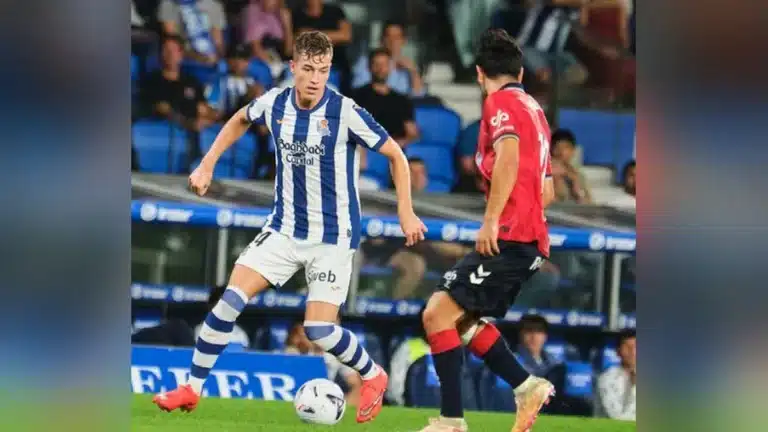 Jugador de la Real Sociedad con el dorsal 24 conduce el balón ante un rival de rojo en Anoeta