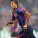 Rodri corre bajo la lluvia con la camiseta del FC Barcelona durante un partido, con un rival del Manchester City desenfocado al fondo