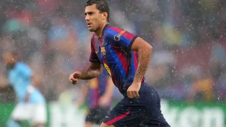 Rodri corre bajo la lluvia con la camiseta del FC Barcelona durante un partido, con un rival del Manchester City desenfocado al fondo