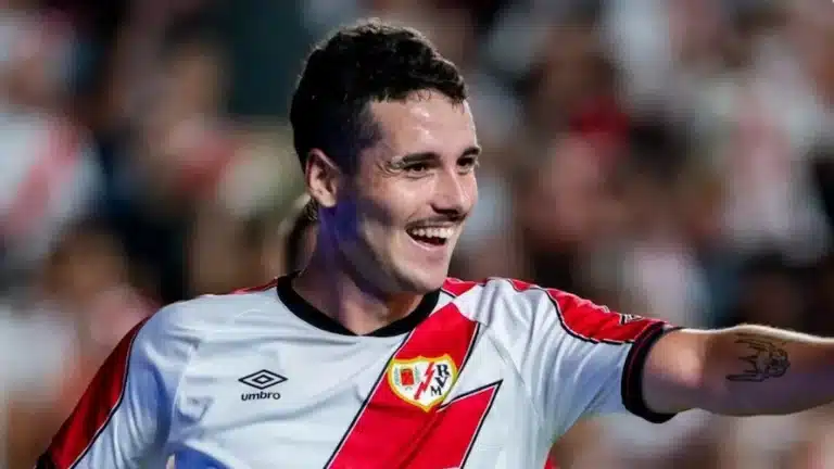 Sergio Camello sonríe y señala con el brazo extendido, con la camiseta del Rayo Vallecano en un partido de LaLiga